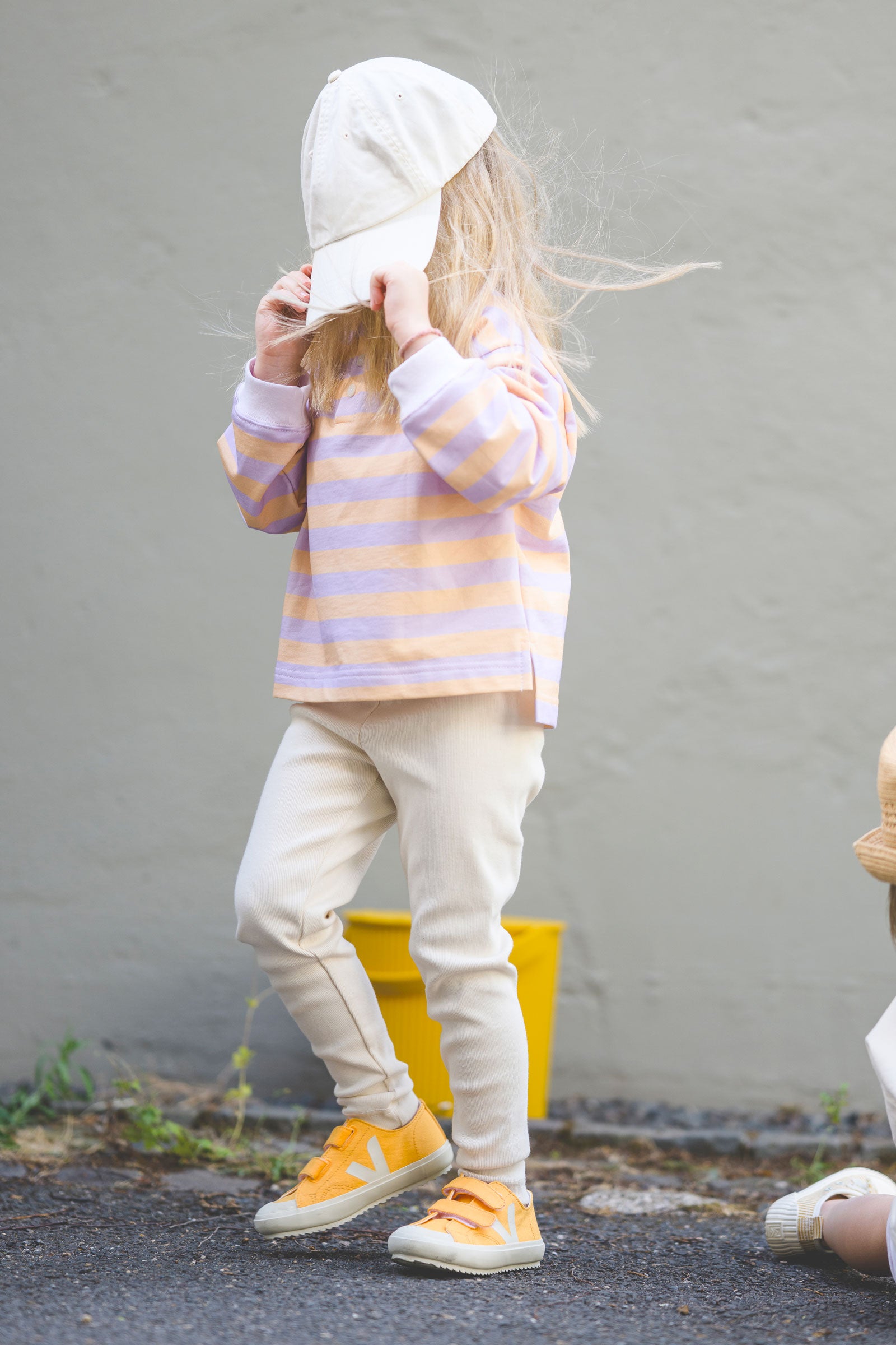 Kind trägt gestreiftes longsleeve in Lavendel und peach mit beigefarbenen leggings
