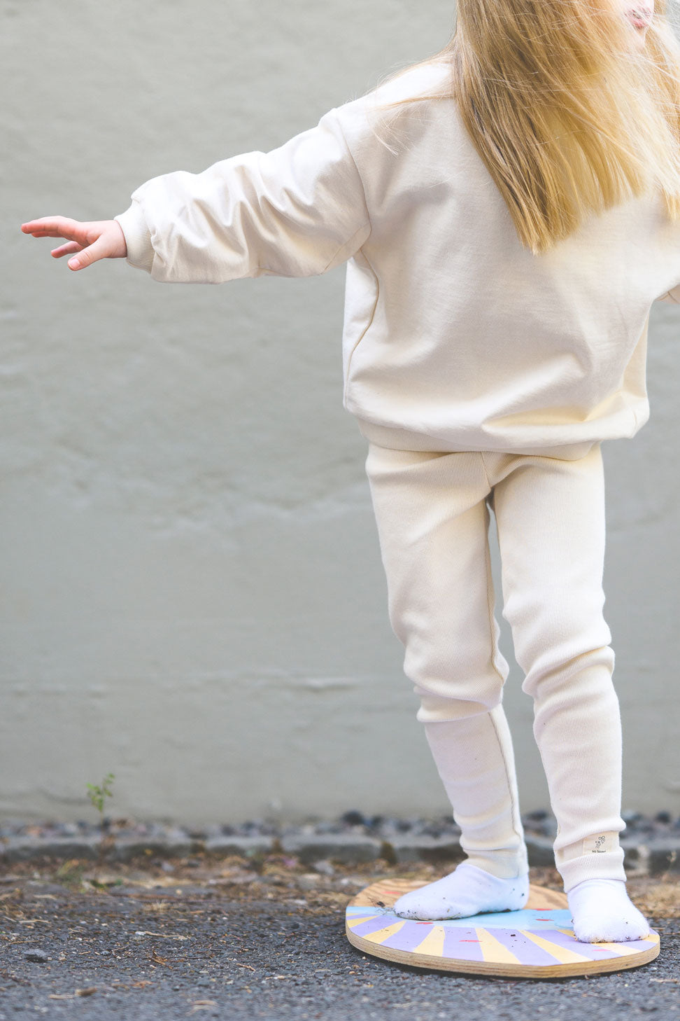 Kind trägt lockere Leggings in hellem beige mit Aufschrift "so loved" und weitem Sweatshirt in hellem beige